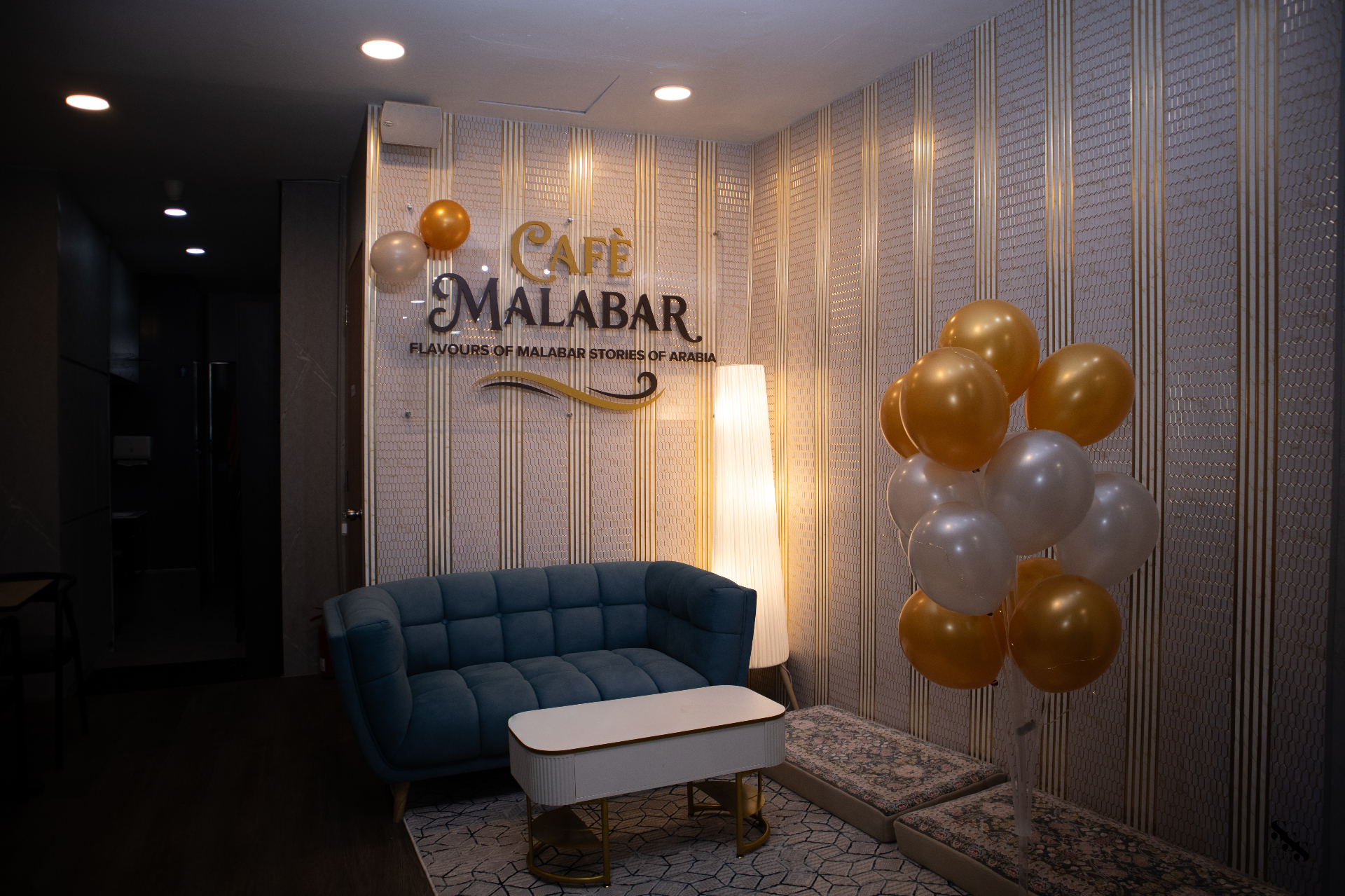 Lounge area at the entrance of Café Malabar with the illuminated logo on a patterned wall